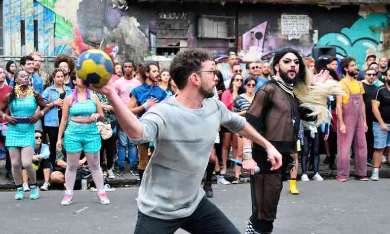 Homem joga bola, na rua, cercado de pessoas fantasiadas durante o jogo gaymada