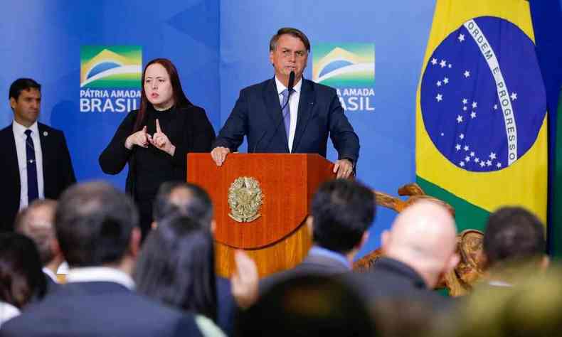 Jair Bolsonaro, no plpito, fala para plateia. A sua esquerda est uma interprete de LIBRAS e a sua direita, a bandeira do Brasil.