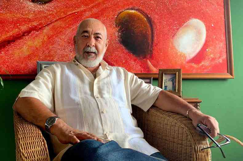 Em sua casa na capital cubana, o escritor Leonardo Padura est sentado em uma cadeira de palha, tendo ao fundo pintura em tons vermelhos