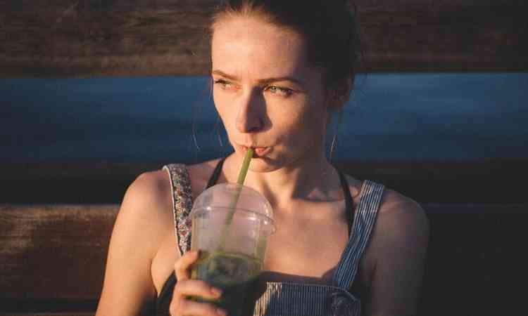 mulher tomando suco verde em copo com canudinho