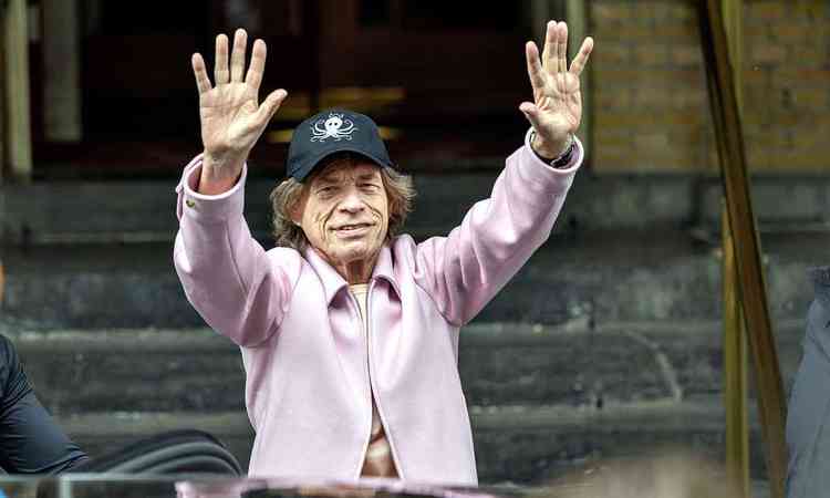 vestindo bon preto e casaco rosa, Mick Jagger ergue os braos e acena para fs na sada de hotel