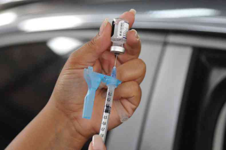 Mo de profissional de sade inserindo seringa em frasco com vacina para aplicar na populao de BH