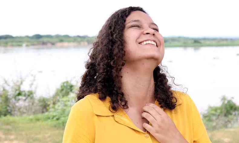 Usando blusa amarela, jovem cineasta Karla Vianely Rodrigues sorri, tendo o céu como cenário
