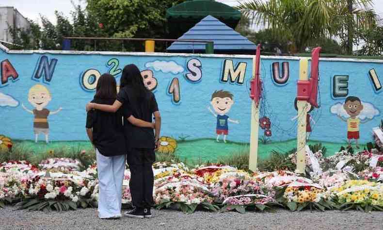 duas pessoas abraadas em frente a creche, em Blumenau, com passeio lotado de homenagens pelas quatro crianas assassinadas