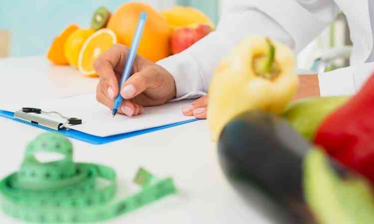 Acompanhamento nutricional; nutricionista receitando dieta; na mesa, algumas frutas e legumes 