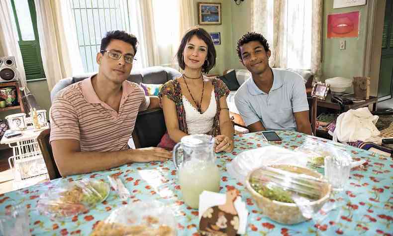 Os atores Christian/Renato (Cauã Reymond), Lara (Andréia Horta) e Ravi (Juan Paiva) sentados em volta de mesa com alimentos na cena de 'Um lugar ao sol'