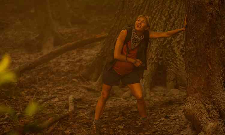 Atriz Sienna Miller encostada ao tronco de rvore olha para cima com expresso assustada