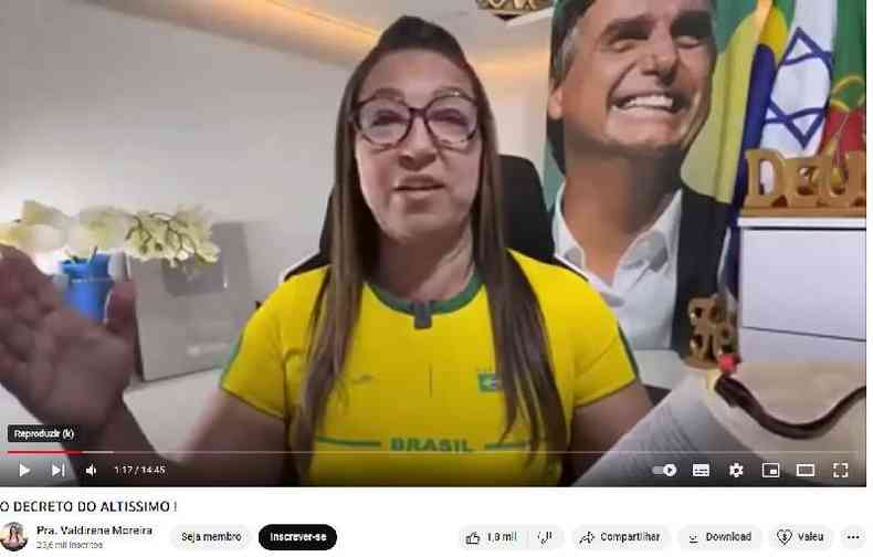Valdirene Moreira sentada em cenrio com bandeiras do Brasil, Portugal e Israel ao fundo, alm de pster com foto de Bolsonaro e placa comemorativa que ganhou do YouTube