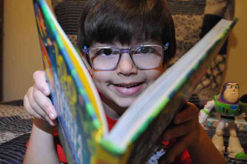 O menino Isaac sorrindo enquanto abre um livro