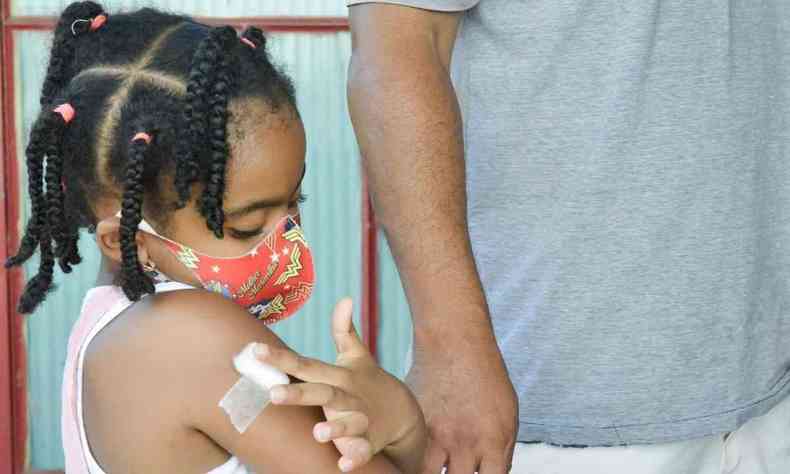 Menina segurando algodão no braço após vacina