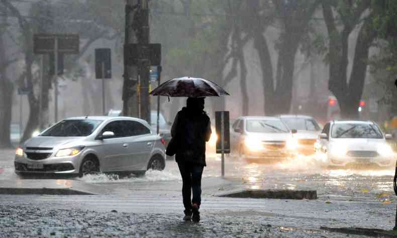 Pessoa com um guarda-chuva durante forte chuva, com carros passando perto