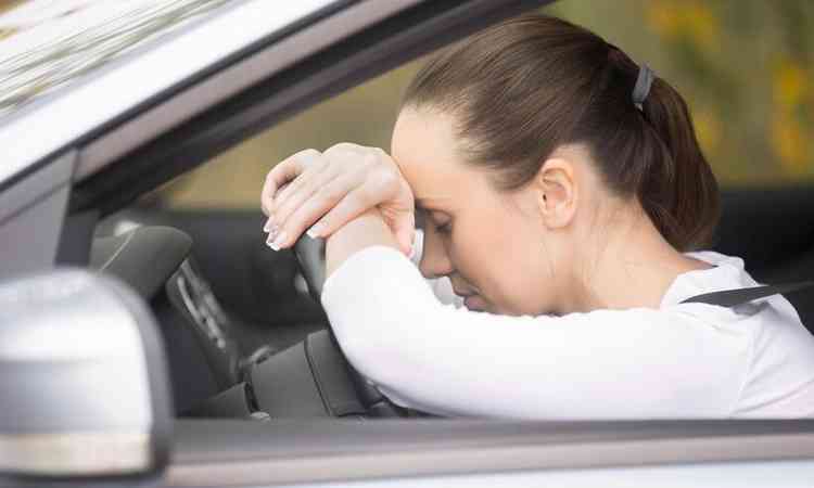 mulher com a cabea no volante do carro, sentindo mal estar