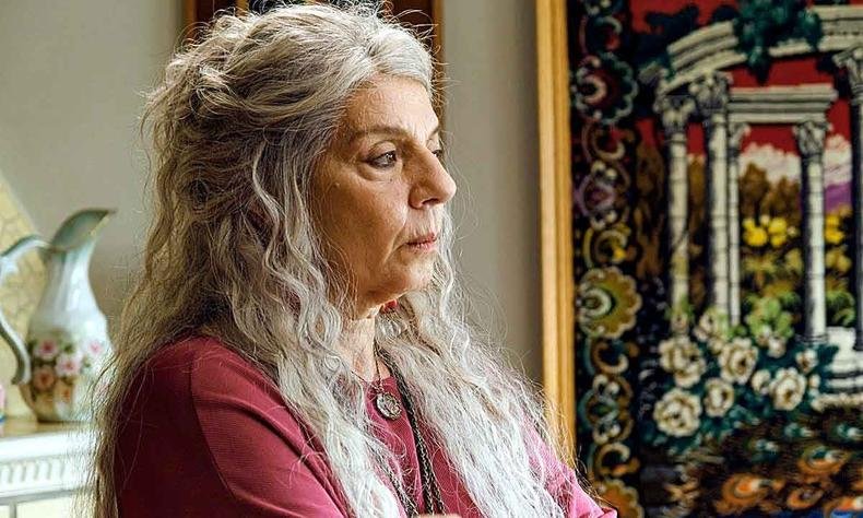 De blusa pink e com longos cabelos brancos, Rosi Campos, de perfil, em cena de no mundo da luna