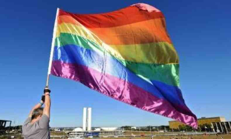 Homem segurando a bandeira LGBTQIA+ com as cores do arco-ris em frente ao prdio do Congresso Nacional
