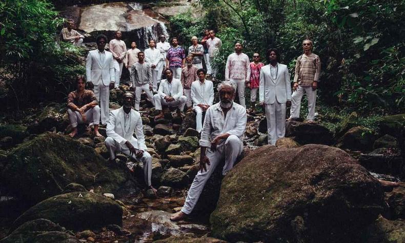 Numa cachoeira, em meio s rvores, o maestro Letieres Leite est  frente, numa pedra. Atrs dele esto msicos da Orkestra Rumpilezz 