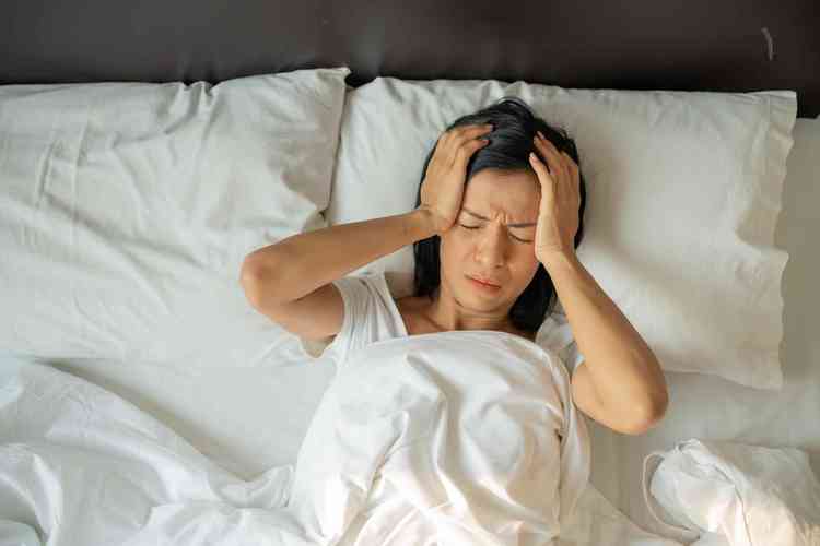 mulher madura exausta e infeliz deitada na cama com os olhos fechados tocando as temporas de perto mulher cansada sofrendo de dor de cabeca ou enxaqueca