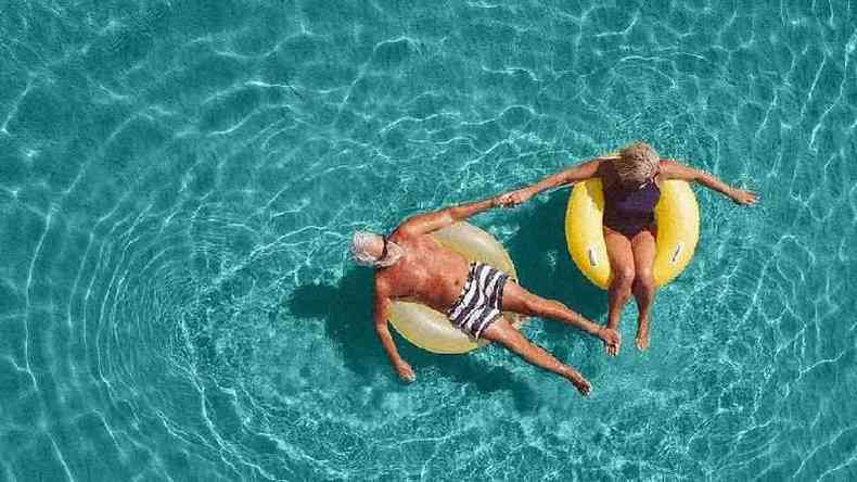 Casal de meia-idade tomando sol em boias na piscina