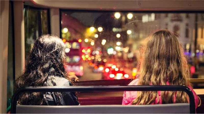 Fotografia colorida mostra duas mulheres em um nibus sentadas de costas