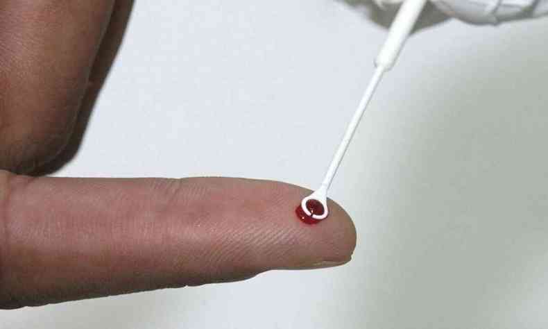 Pessoa tendo dedo espetado para realizar exame de sangue