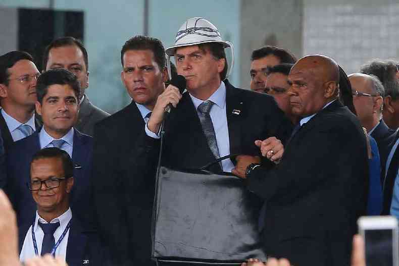 Jair Bolsonaro dando entrevista. Ele usa um chapu nordestino de couro branco e um terno preto. Tambm segura um microfone e est rodeado de assessores.