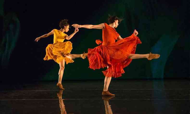 Bailarinas do Grupo Corpo danam no palco, vestindo figurinos laranja e vermelho