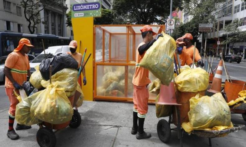Coletadores de lixo com vrios sacolas cheias de resduos, alm do que j esto dentro do lixmetro, uma gaiola de vidro onde so armazenados os lixos 