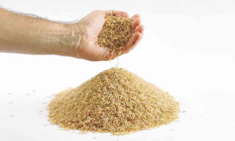 Mo masculina despeja arroz integral em mesa j coberta por este cereal 