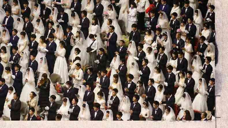 Foto de cima mostra dezenas de casais amarelos - noivos de terno e noivas de branco - que olham para a mesma direo 