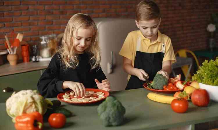 um casal de crianças na cozinha preparando alimentos saudáveis