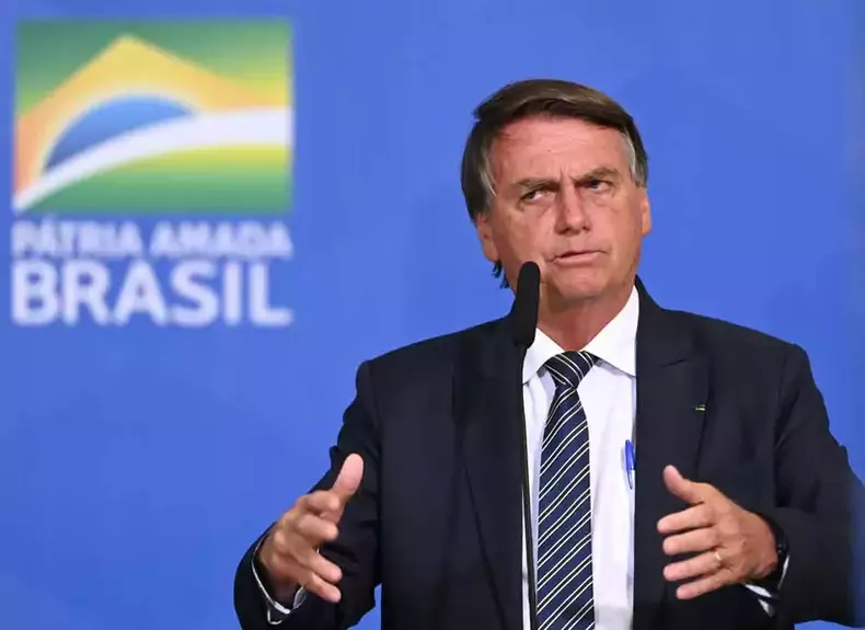 Bolsonaro gesticula com as mos diante de microfone com fundo azul e bandeira do Brasil 