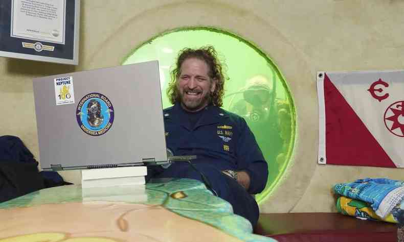 Professor em sua residncia sub-aqutica com cama, computador e mergulhador na janela