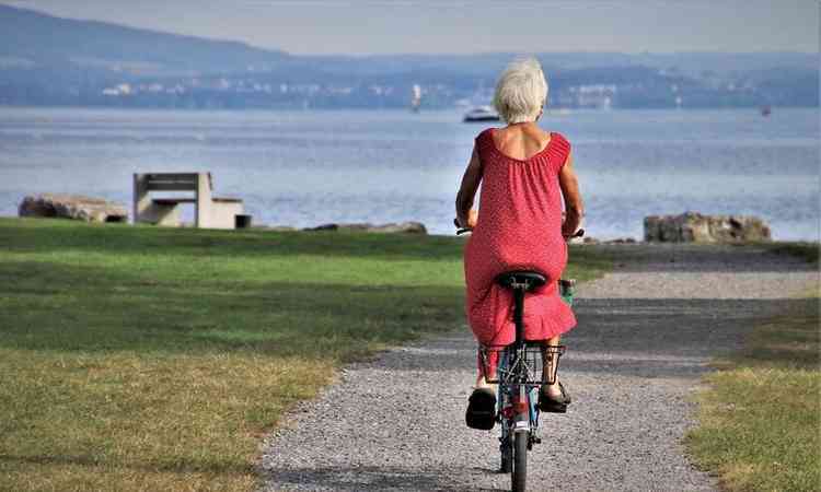 senhora, de cabelos brancos, anda de bicicleta em direo ao mar