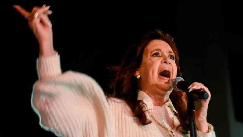 Kirchner gesticula enquanto fala no microfone, em evento  noite