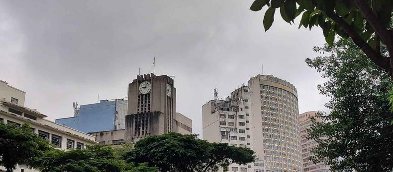 Relgio da Prefeitura de BH e prdios do centro ao fundo. Cu nublado, e rvores ao redor da imagem 