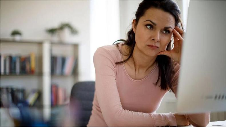 Mulher branca de cabelo preto est sentada em frente ao computador com a mo nas tmporas