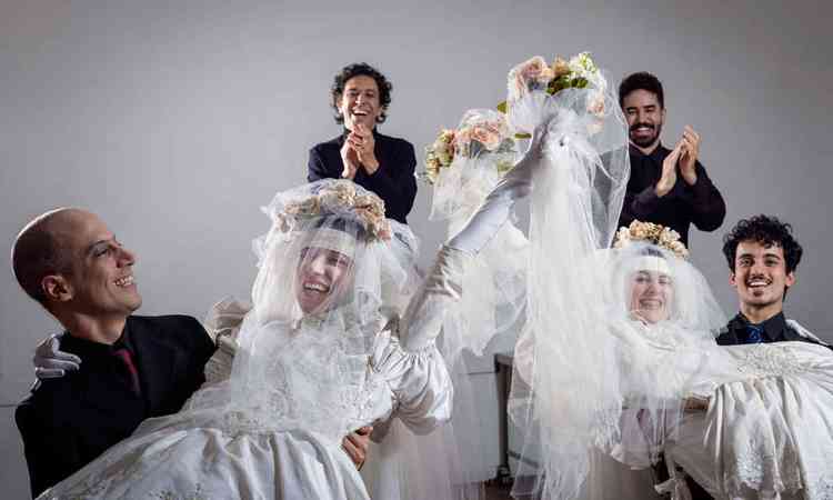 Duas atrizes vestidas de noiva e atores com figurinos de casamento sorriem para a cmera
