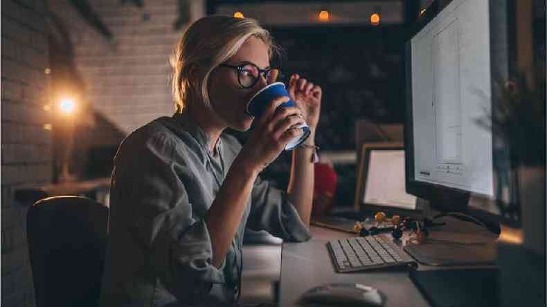 Uma mulher tomando café e olhando para uma tela de computador