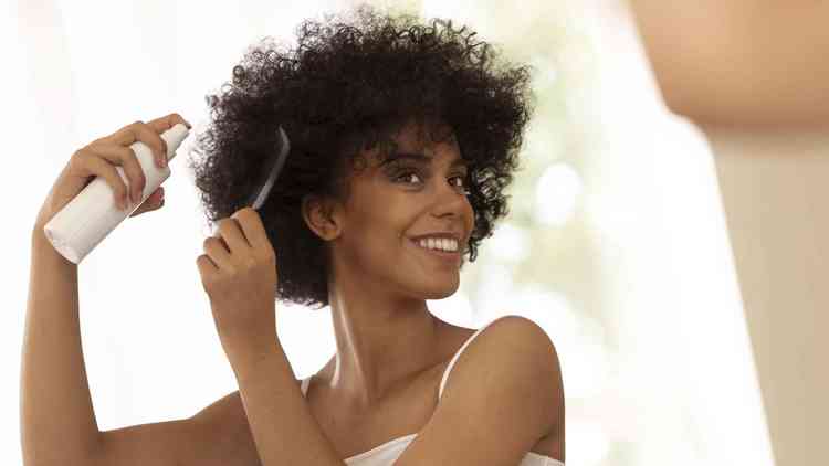 mulher negra sorridente usando produto de cabelo em seu cabelo cacheado