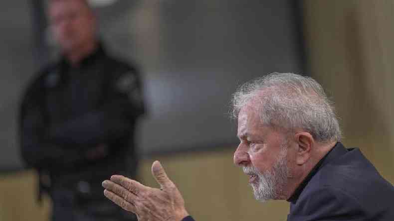 O ex-presidente Lula aparece de perfil falando, com agente de segurana no plano de fundo