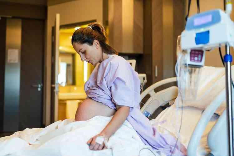 Mulher grvida sentada em cama de hospital prestes a dar a luz