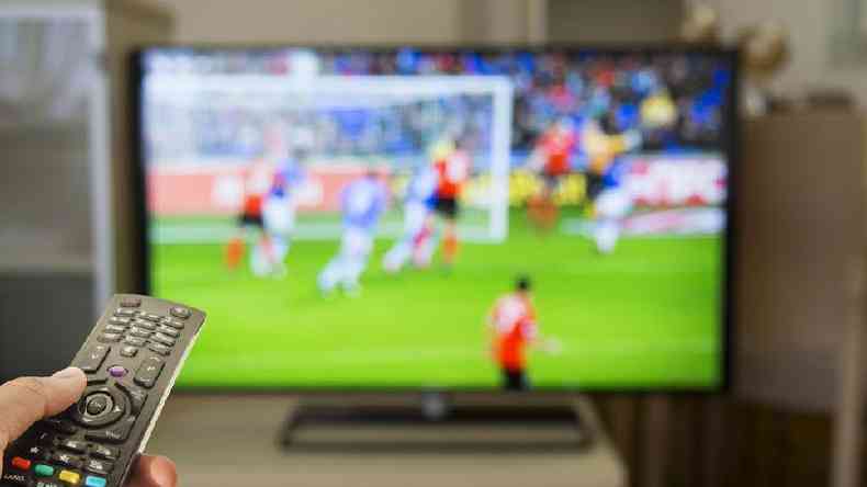 Controle remoto com televiso passando futebol desfocada ao fundo