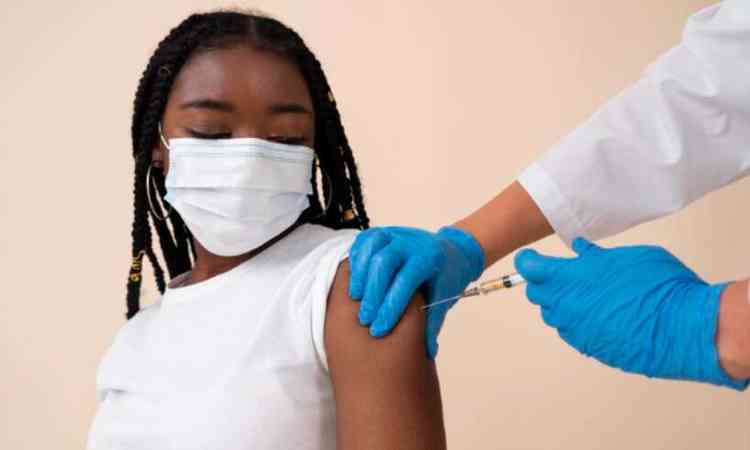 Menina negra de mscara tomando vacina no brao