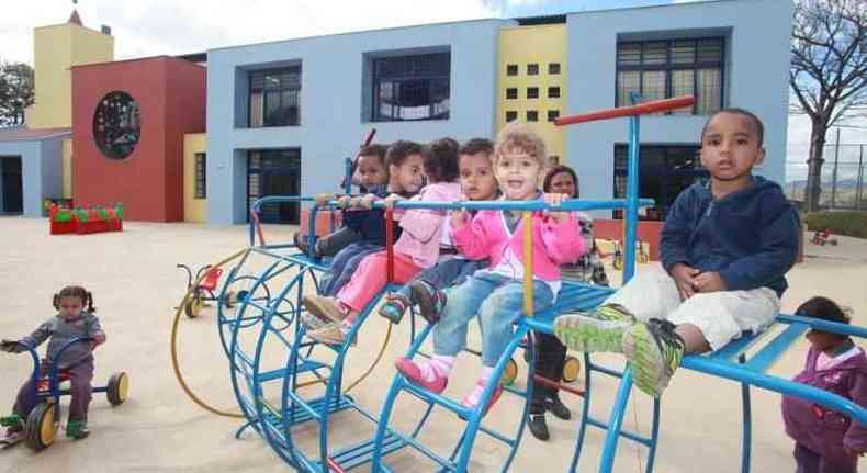 Quatro meninas e quatro meninos brincam no parquinho de uma escola municipal de BH, acompanhados por uma monitora.