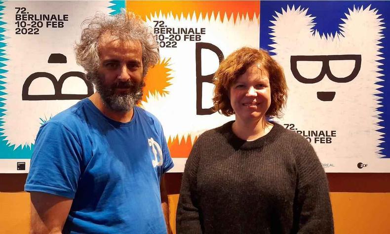 Adirley Queirós e Joana Pimenta apostam na 'etnografia da ficção'(foto: Reprodução) Diretores Adirley Queirós e Joana Pimenta sorriem, ao fundo vêem-se cartazes do festival de cinema de Berlim