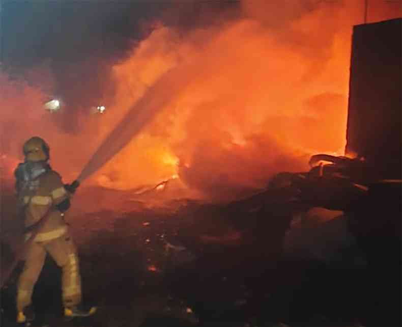 Bombeiro combate com mangueira de incndio a fogo chamas em galpo de reciclagem  noite em Contagem