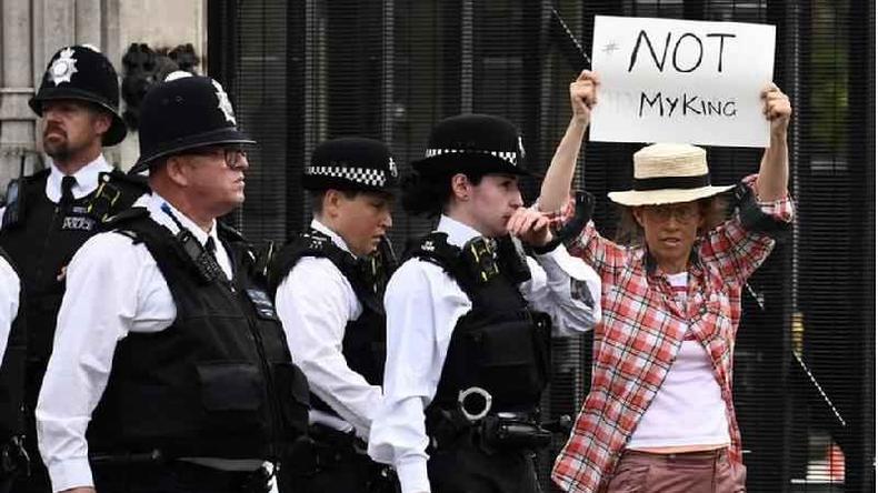 Manifestante segura cartaz onde se lê 'não é o meu rei' em inglês. O apoio à monarquia vem caindo, mas ainda existe entre a maioria da população(foto: Getty Images) Fotografia colorida mostra uma pessoa branca de óculos segurando um cartaz escrito 'not my king', ou 'não é meu rei' em inglês, ao lado de pessoas com fardas (em frente ao palácio de Westminster).