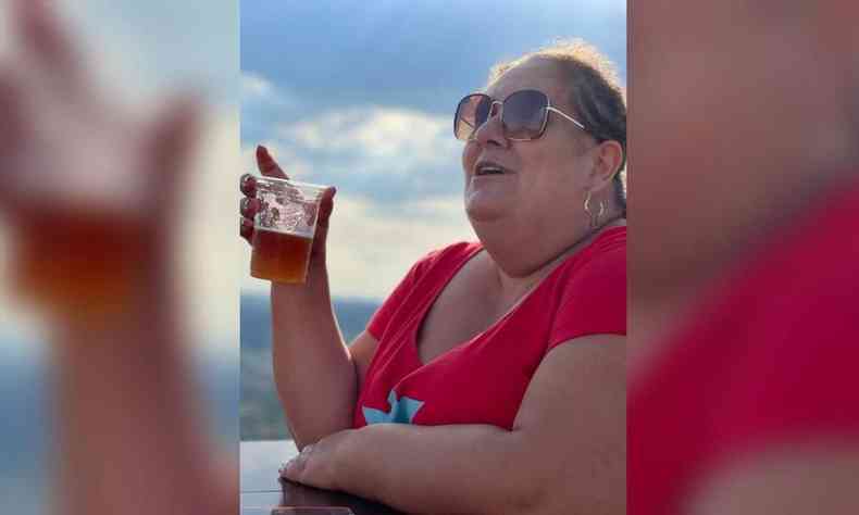 Jéssica Balbino com um copo de cerveja. Ela veste blusa vermelha e usa óculos