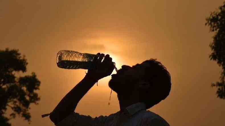 Um homem bebe água de uma garrafa com o sol ao fundo