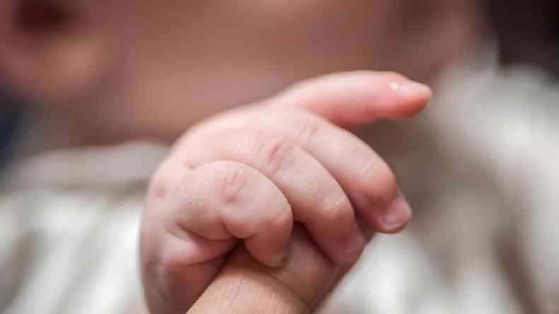 Um beb pegando o dedo indicador de um adulto