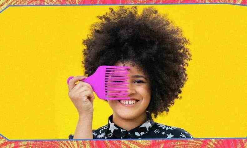 Paula Silva  uma mulher negra de cabelos crespos. Ela segura um pente garfo rosa em frente aos seus olhos